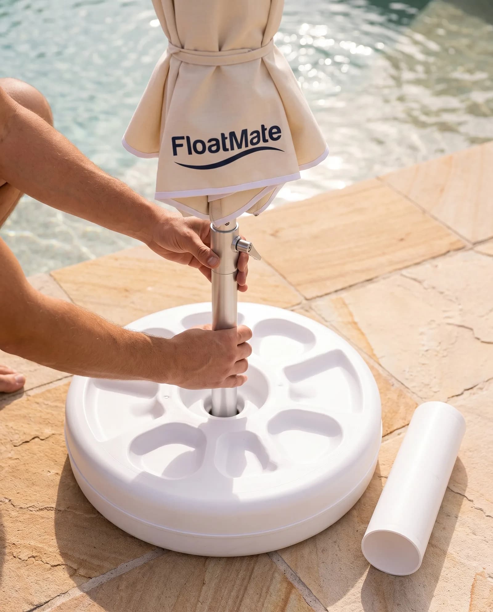 Hands sliding the silver umbrella pole into the centre of the white floating base on the pool paving